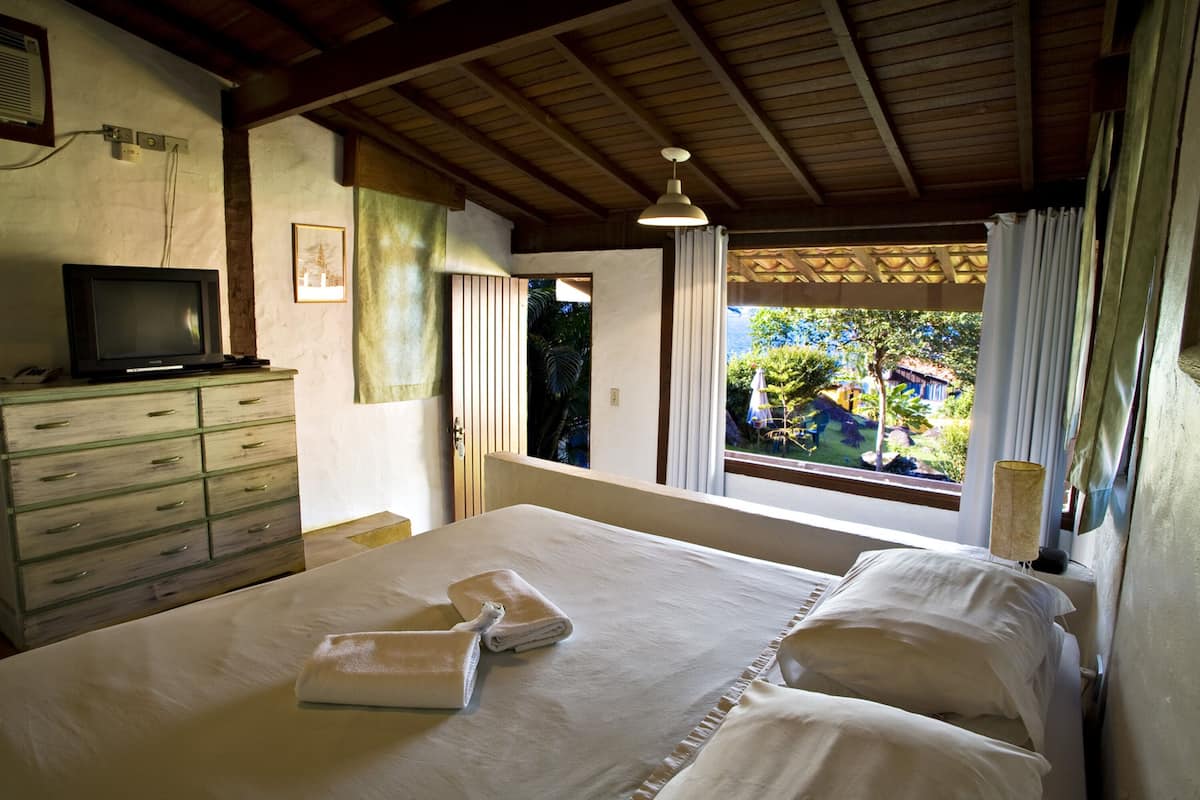 Un dormitorio con cama, cómoda, televisor y ventana con cortinas.