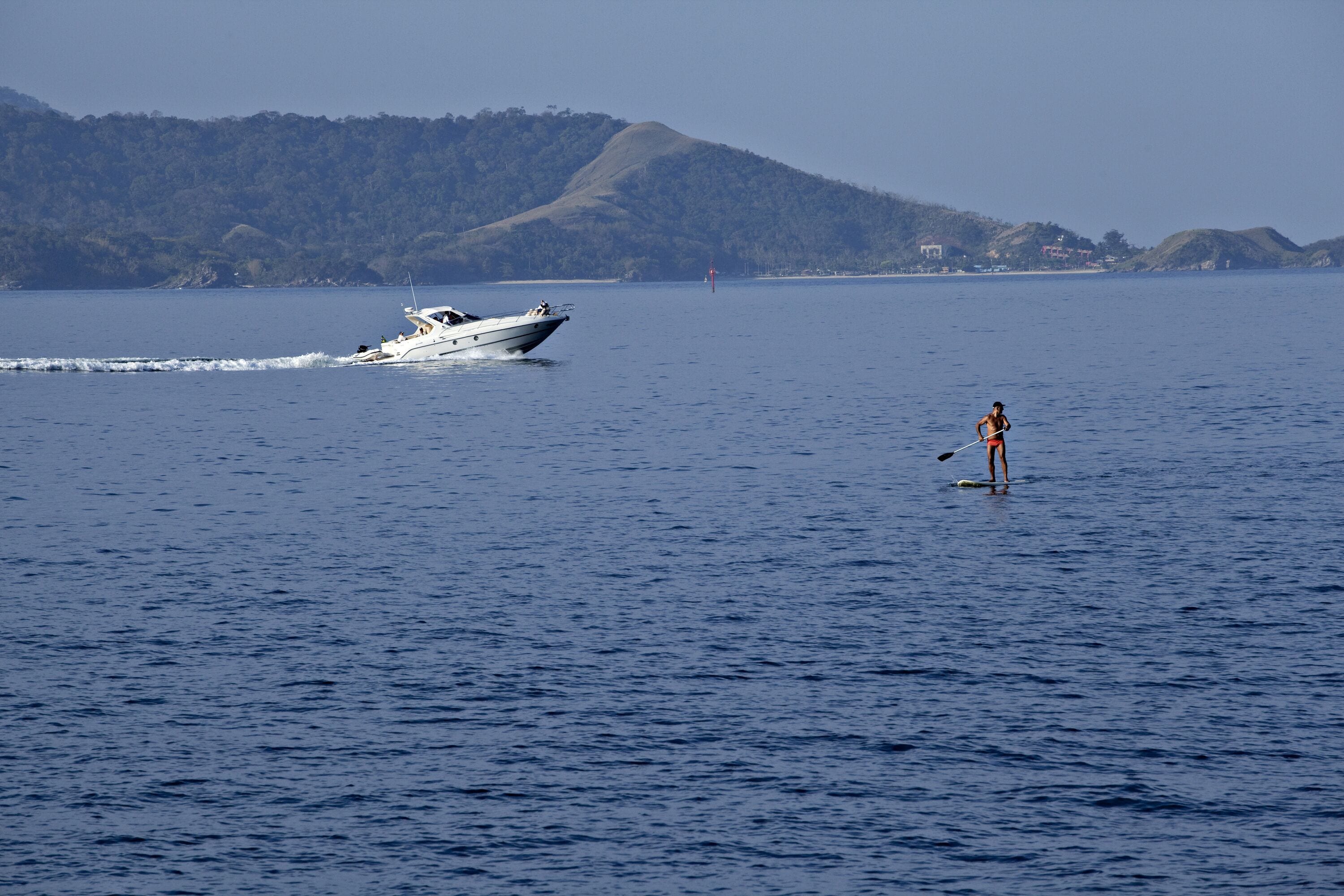 Un bote sobre aguas tranquilas, con una persona haciendo paddleboarding cerca.