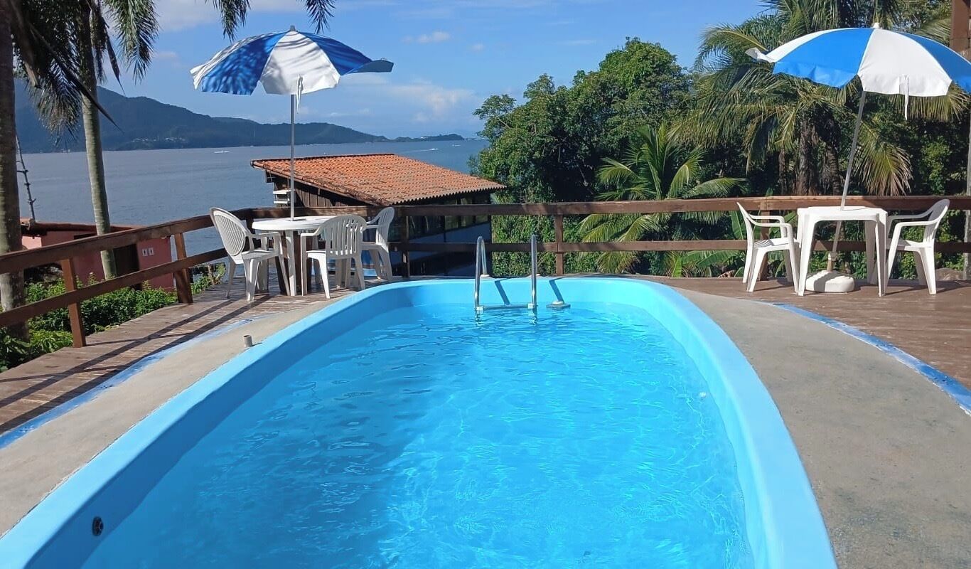 A swimming pool with a wooden deck, white chairs, and umbrellas.