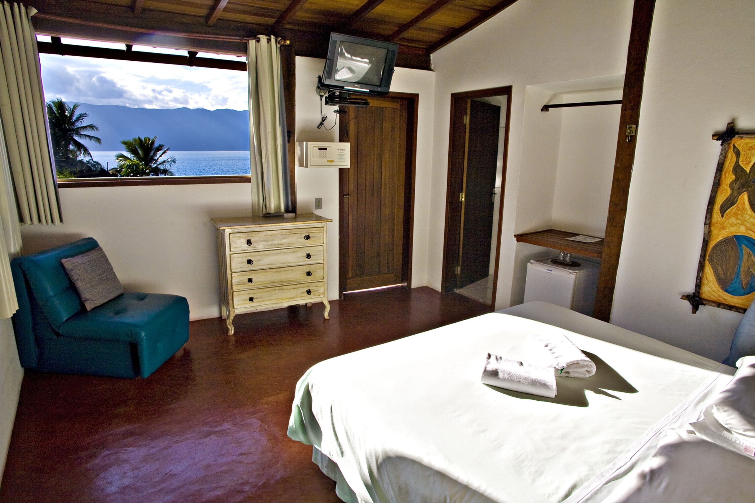 Un dormitori amb un llit, un aparador, un televisor i vista a l'oceà.