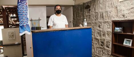 A reception desk with a blue counter, a stone wall, and a wooden shelf with framed pictures.