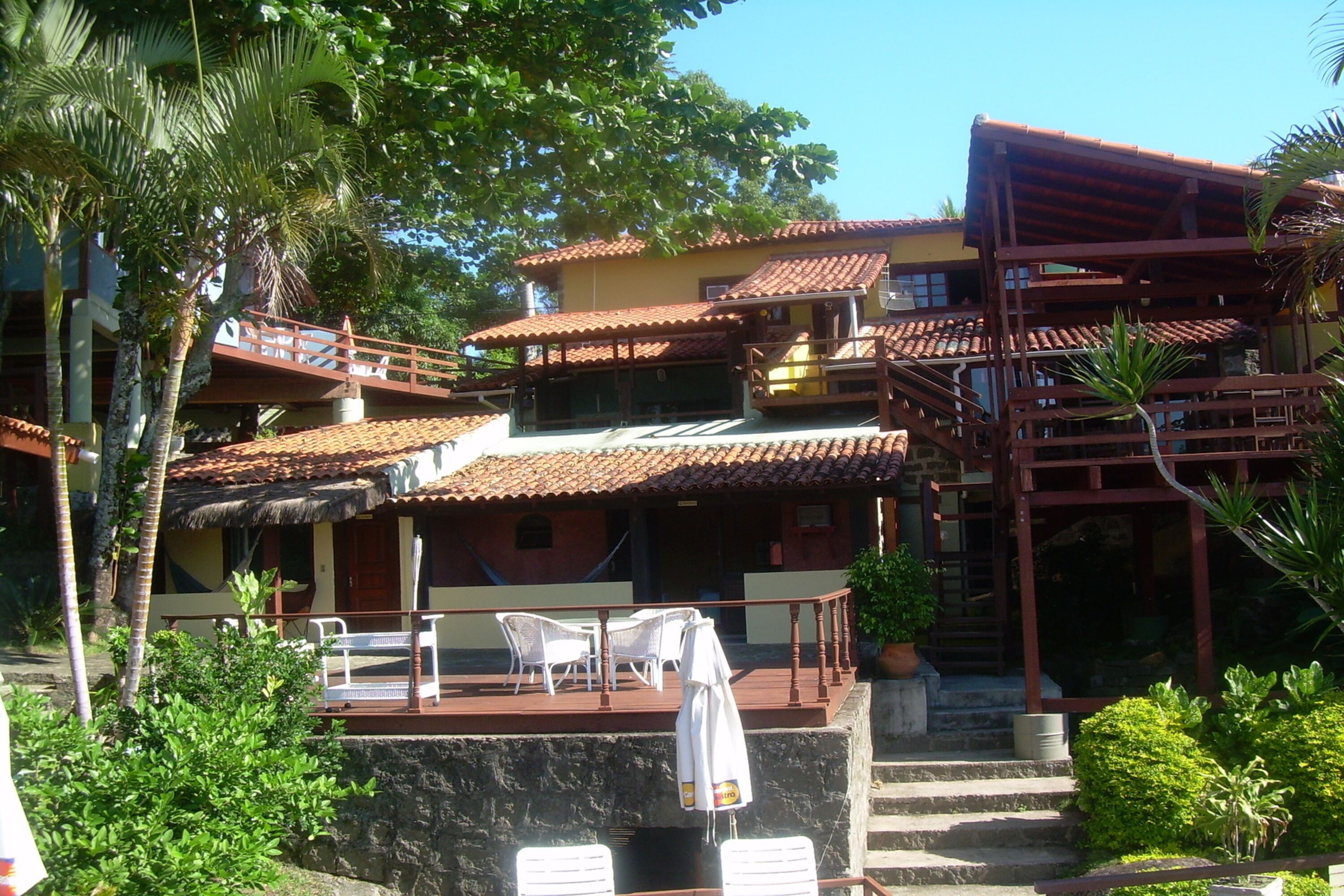A multi-story building with a red-tiled roof, a balcony with white chairs, and a staircase leading to an upper level.