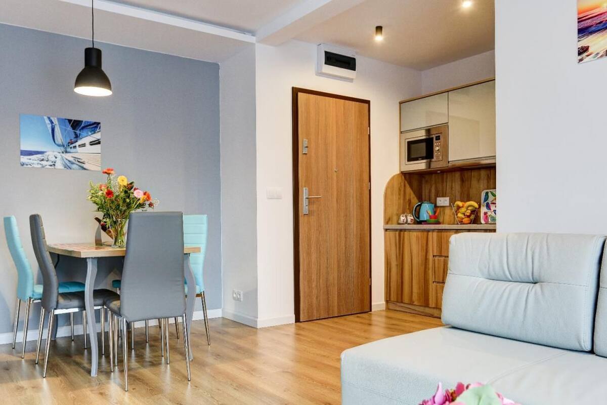 Una sala moderna con un sofá, un comedor con sillas y una mesa, una puerta de madera y un área de cocina con microondas.