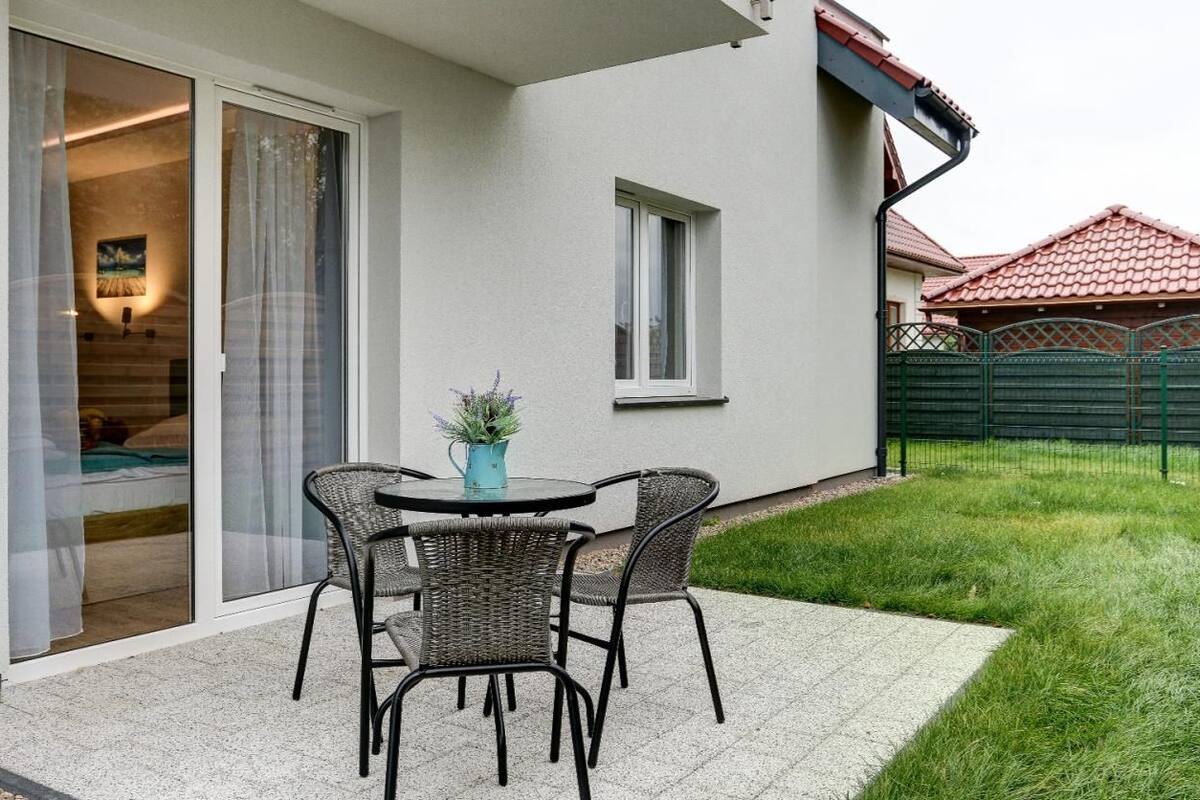 Un patio con una mesa y sillas, una pequeña planta en maceta y un ventanal corredero que da a una habitación.
