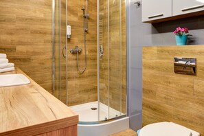 A modern bathroom with a wooden floor, a glass shower enclosure, a white sink, and a toilet.
