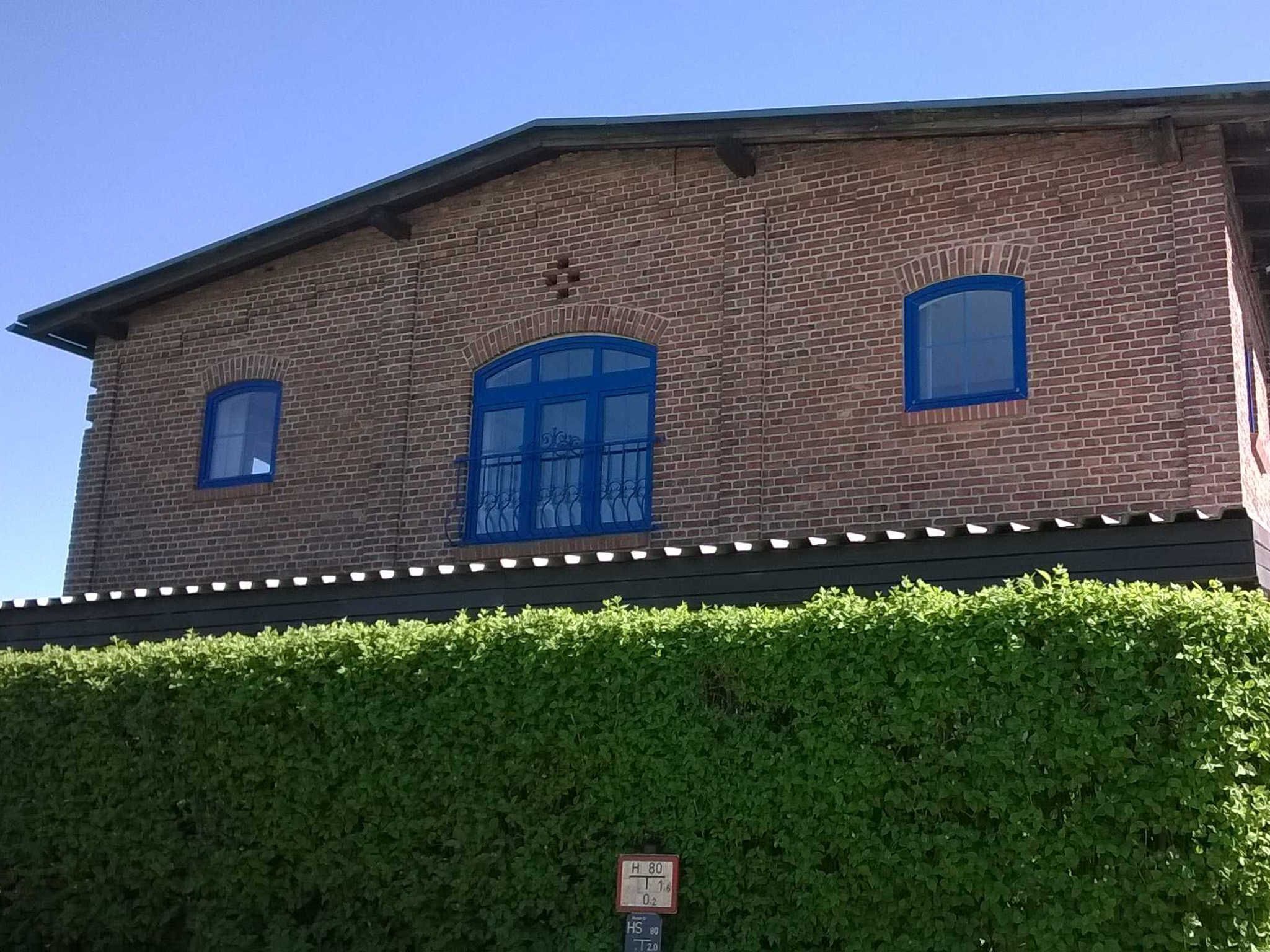 Um edifício de tijolos com três janelas, uma emoldurada em azul e duas com moldura padrão.