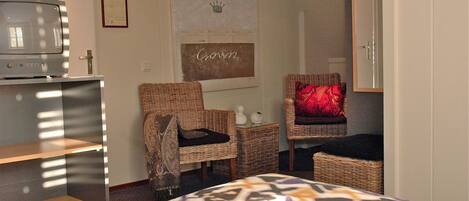 A hotel room with a bed, two wicker chairs, a television, and a framed picture on the wall.