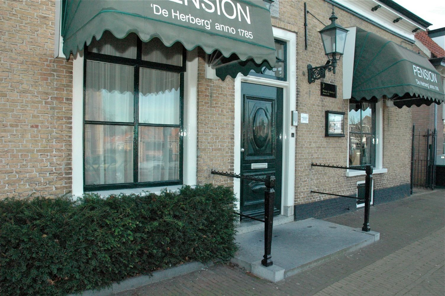 A brick building with a green awning labeled 'Pension De Herberg anno 1785'.