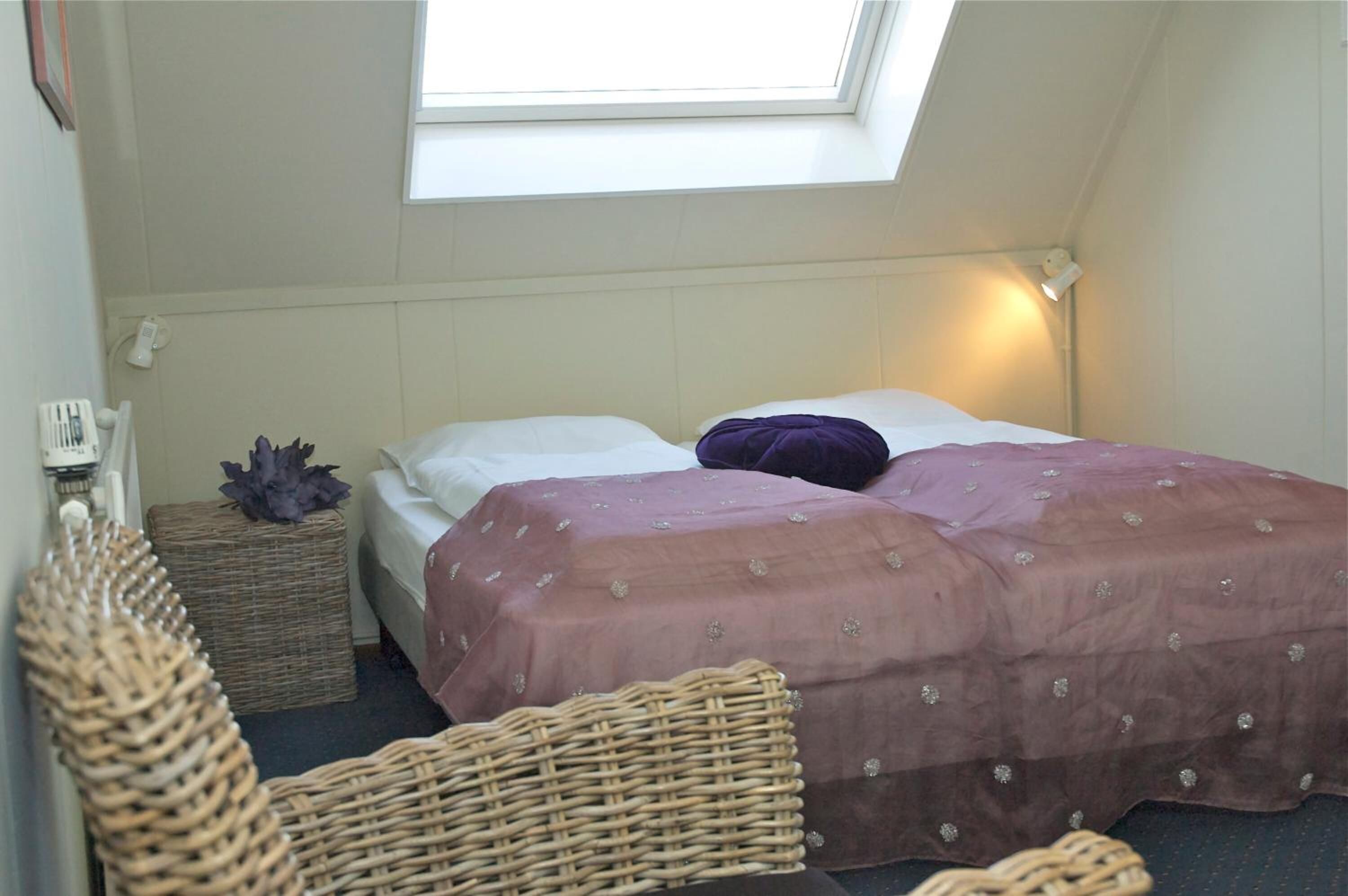 A bedroom with a single bed, a small bedside table, a nightstand, and a window providing natural light.