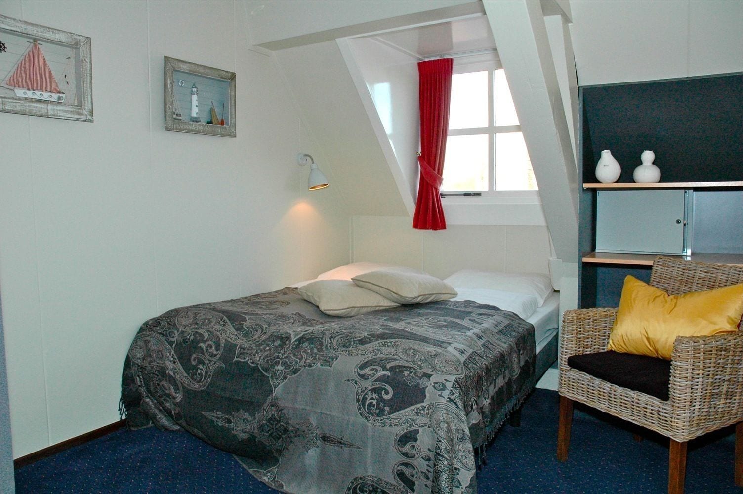 A bedroom with a bed, a chair, a shelf with vases, and a window with a red curtain.