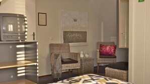 A hotel room with a bed, two wicker chairs, a small table, a television, and a framed picture on the wall. - De Herberg (Renesse)