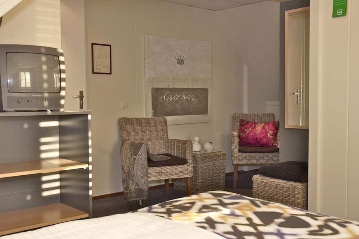 A hotel room with a bed, two wicker chairs, a small table, a television, and a framed picture on the wall.