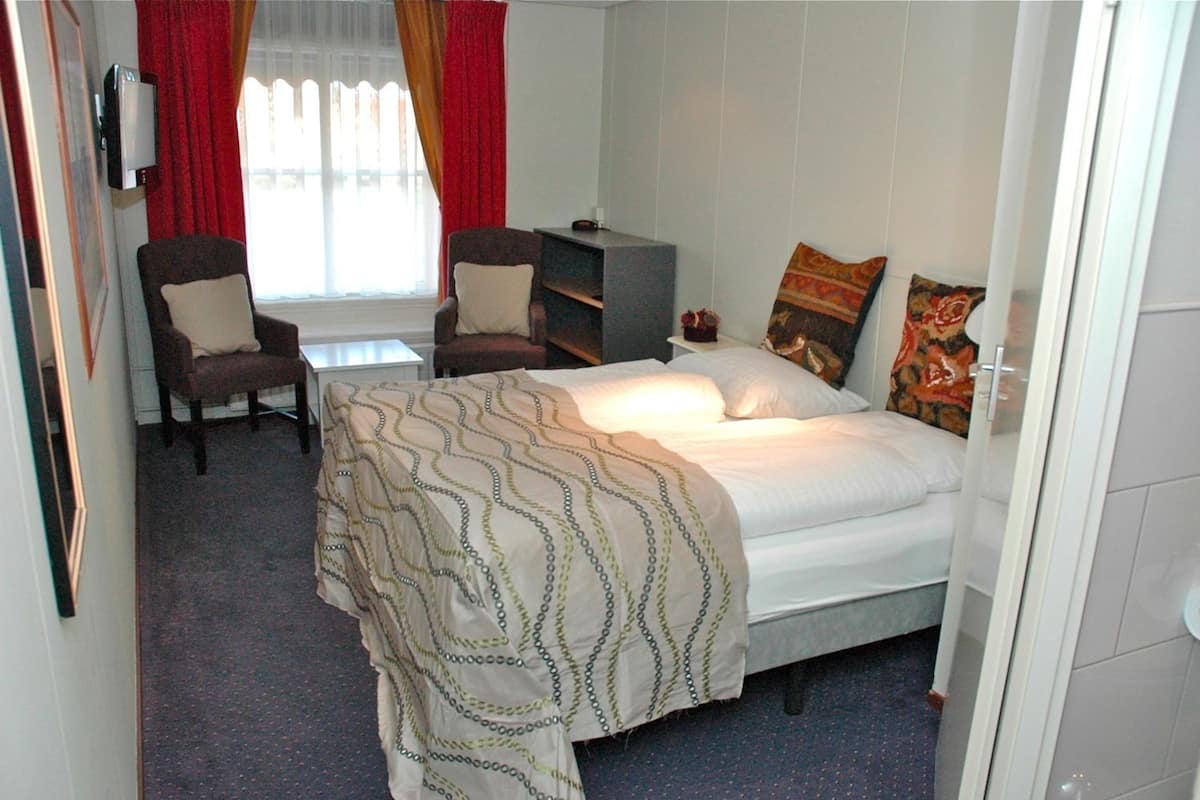 A hotel room with a bed, two chairs, a desk, and a TV.