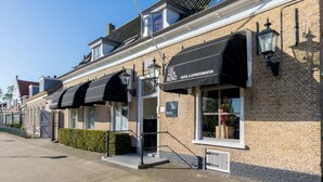 A hotel named "De Her Berg" with a brick facade, black awnings, and a visible entrance. - De Herberg (Renesse)
