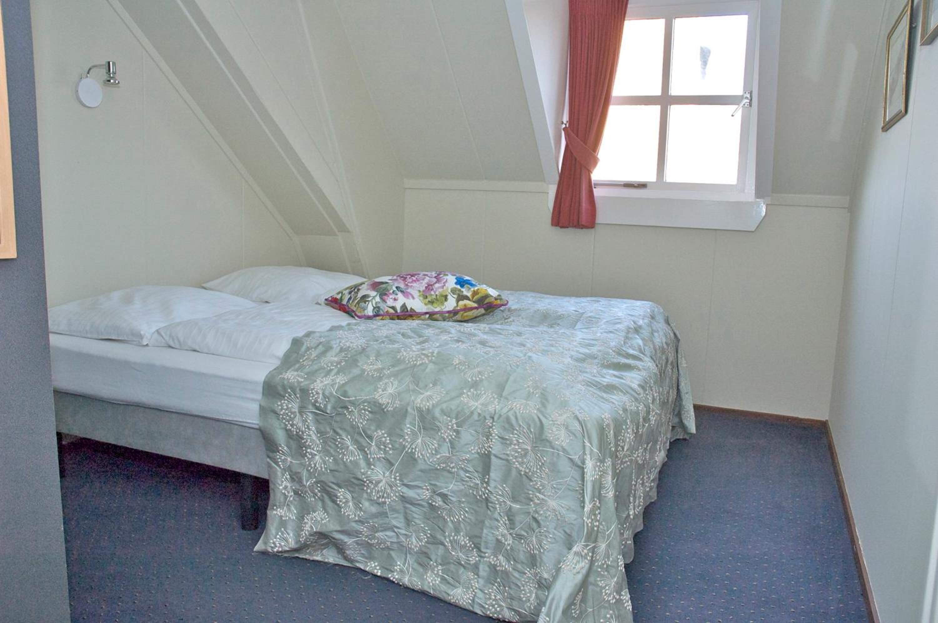 Een slaapkamer met een enkel bed, een raam met gordijnen en een wandlamp.