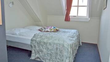 Een slaapkamer met een enkel bed, een raam met gordijnen en een wandlamp.