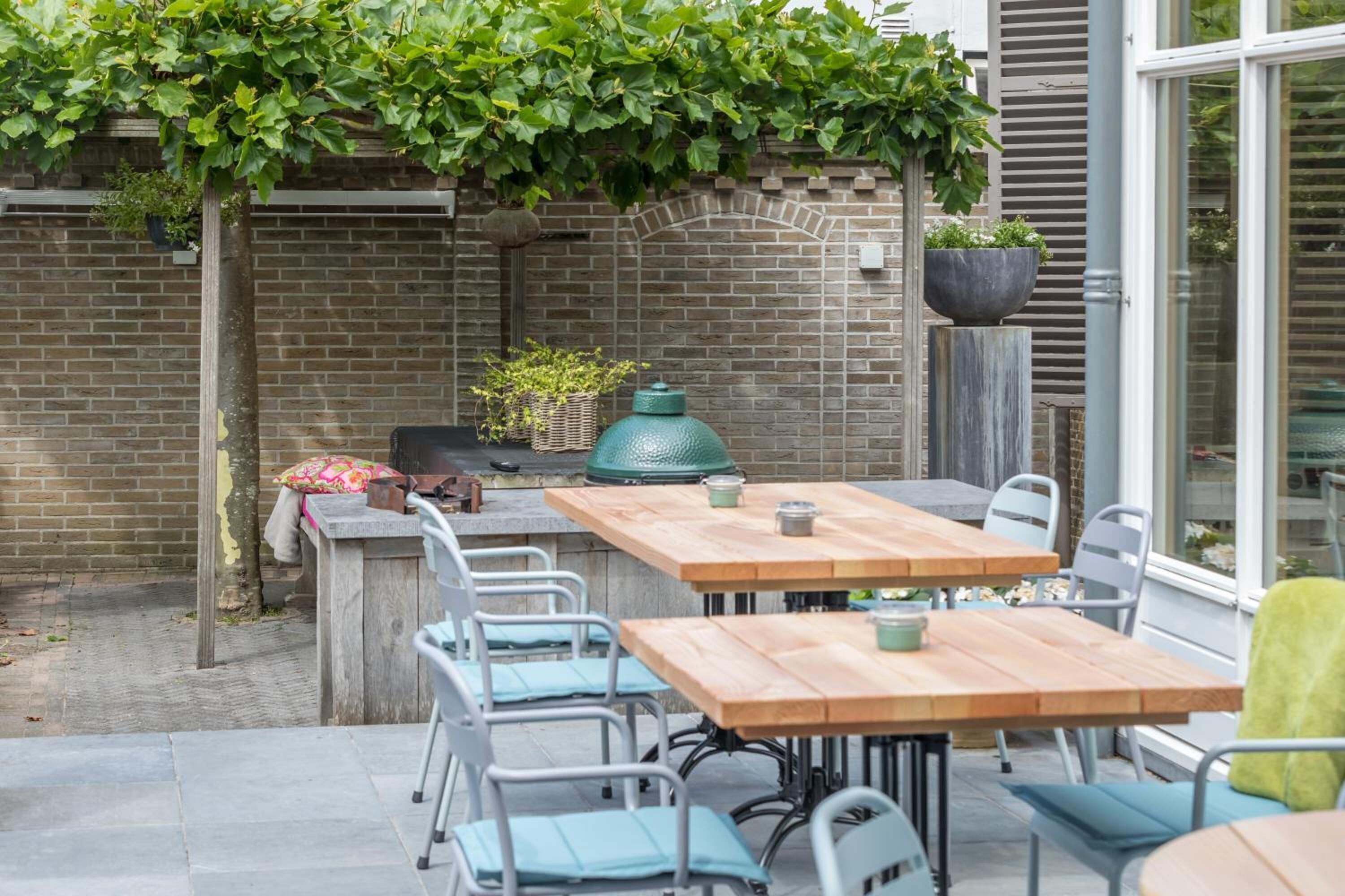 Une terrasse extérieure avec une table et des chaises en bois, un barbecue et un mur en briques.