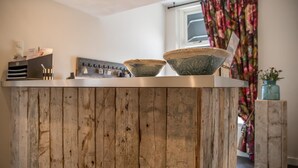 A kitchen with a wooden island, two bowls, and a window with floral curtains. - De Herberg (Renesse)