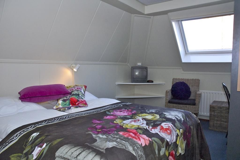 A bedroom with a bed, a television, a wicker chair, and a skylight.