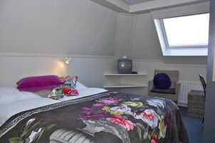 Un dormitorio con cama, televisión, silla de mimbre y tragaluz.