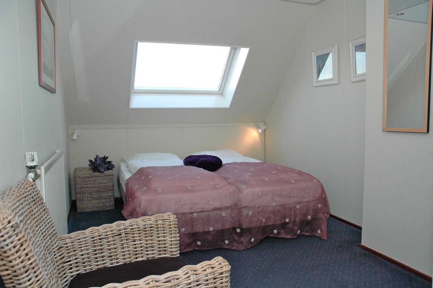A bedroom with a single bed, a small table, a wicker chair, and a skylight.
