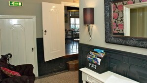 A hotel lobby with a reception desk, a post box, a door, and a dining area in the background. - De Herberg (Renesse)