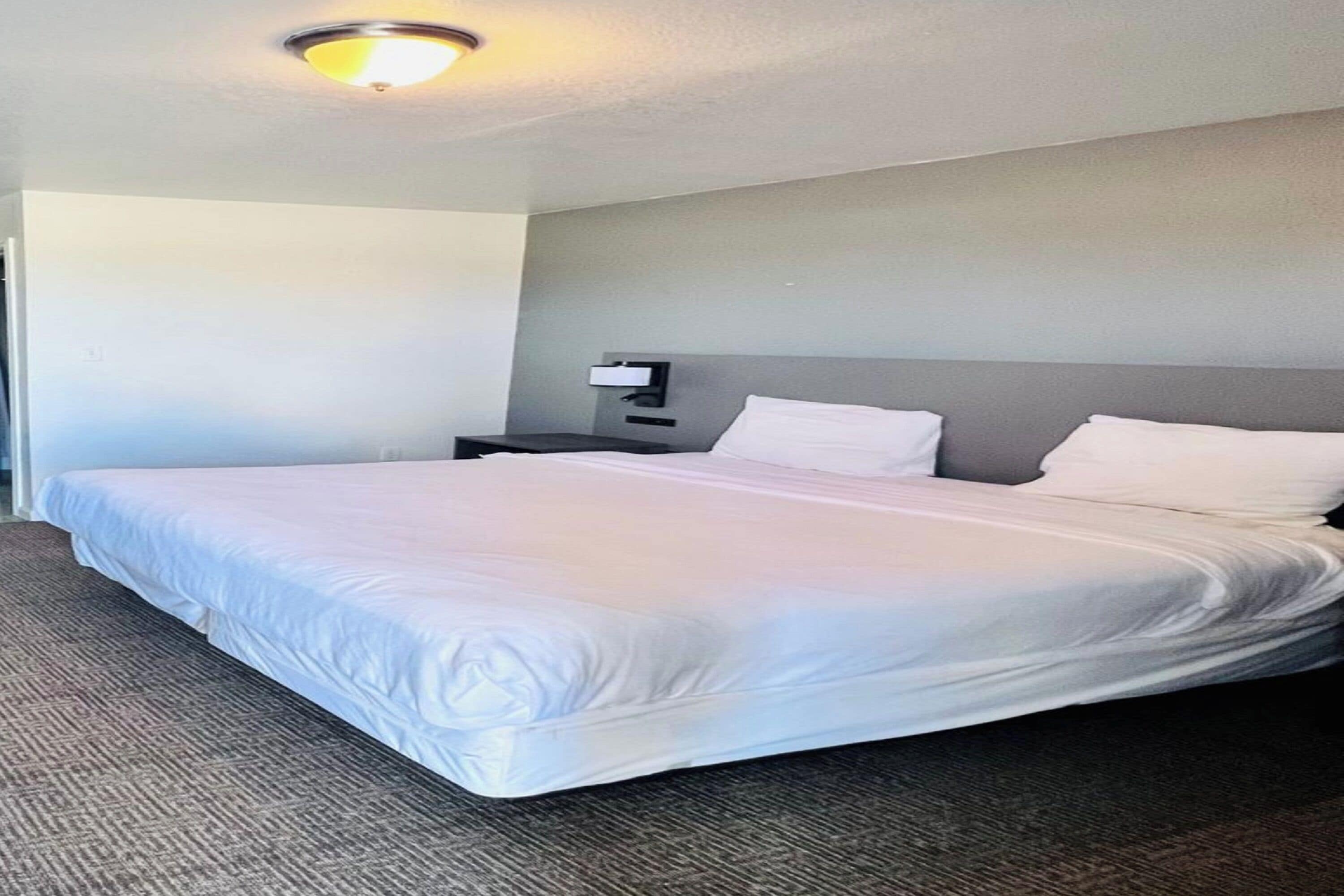 A hotel room with a large bed, a nightstand, and a wall-mounted lamp.