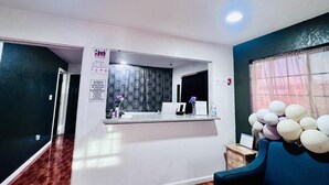 Una zona de recepción con mostrador, una silla azul y un ventanal con cortinas.