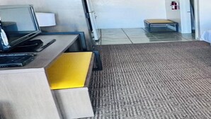 Habitación de hotel con escritorio, una silla, cama, una mesita y extintor.