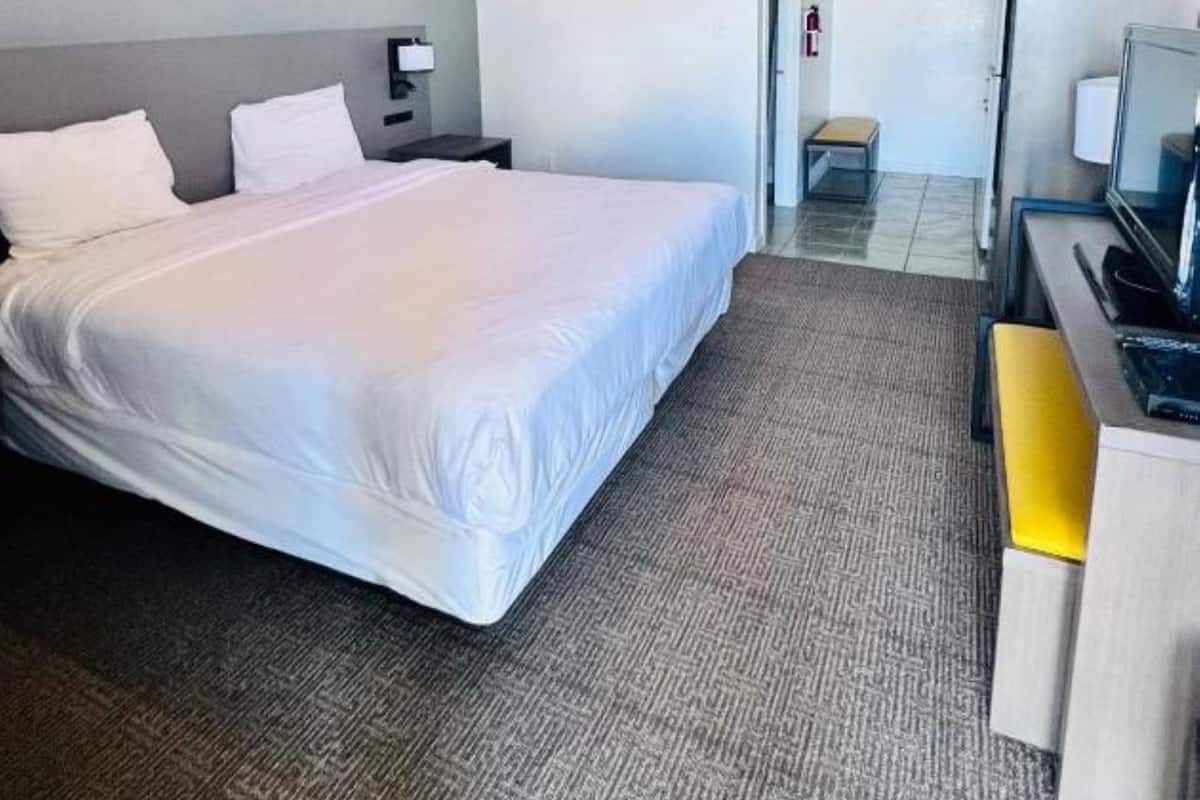 Une chambre d’hôtel avec un grand lit, un bureau avec une chaise, une télévision et un petit tabouret.