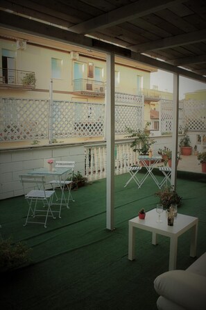 A covered outdoor patio with a green artificial turf floor, white metal chairs, a small round table, and potted plants. - B&B San Peter's Golden Rooms (Rome)
