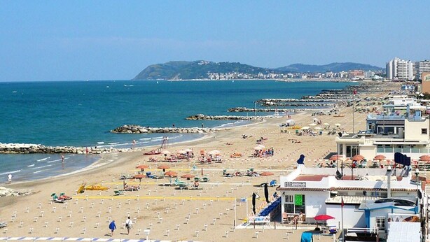 A beach with umbrellas, a restaurant, and a view of the sea and hills. - Hotel Hamilton (Misano Adriatico)