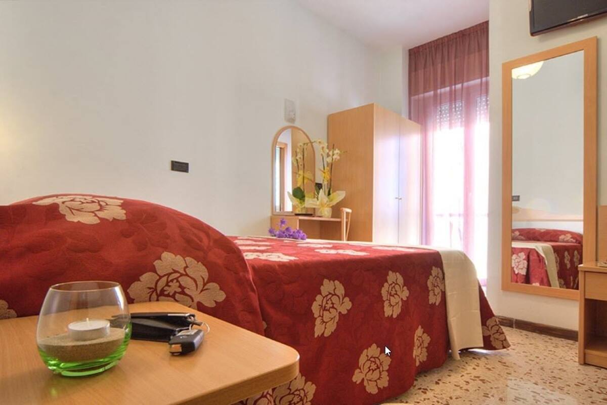 A hotel room with a bed, a desk, a mirror, and a window with curtains.