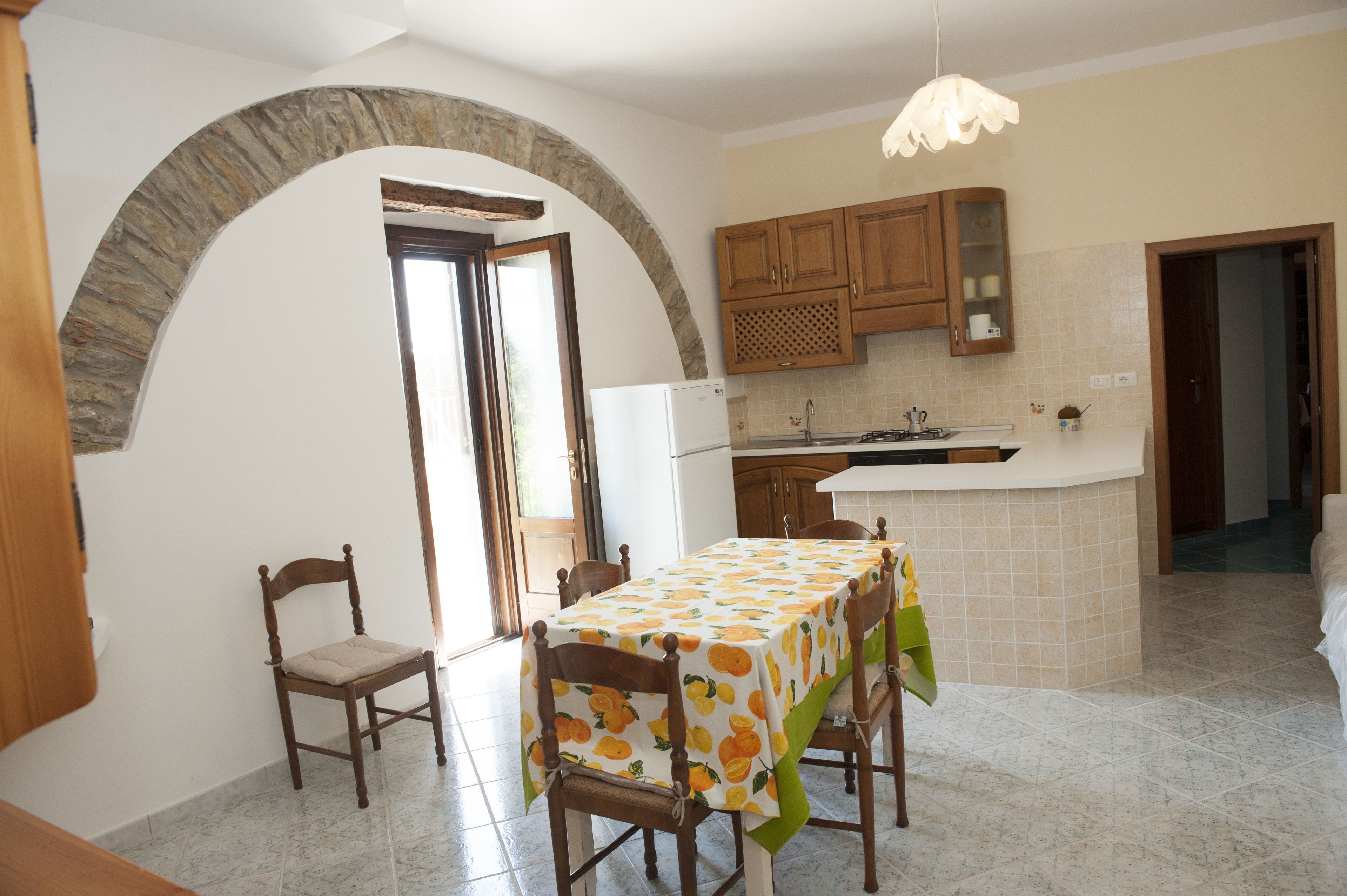 A kitchen with a dining area, stone archway, wooden cabinets, and a tiled floor.