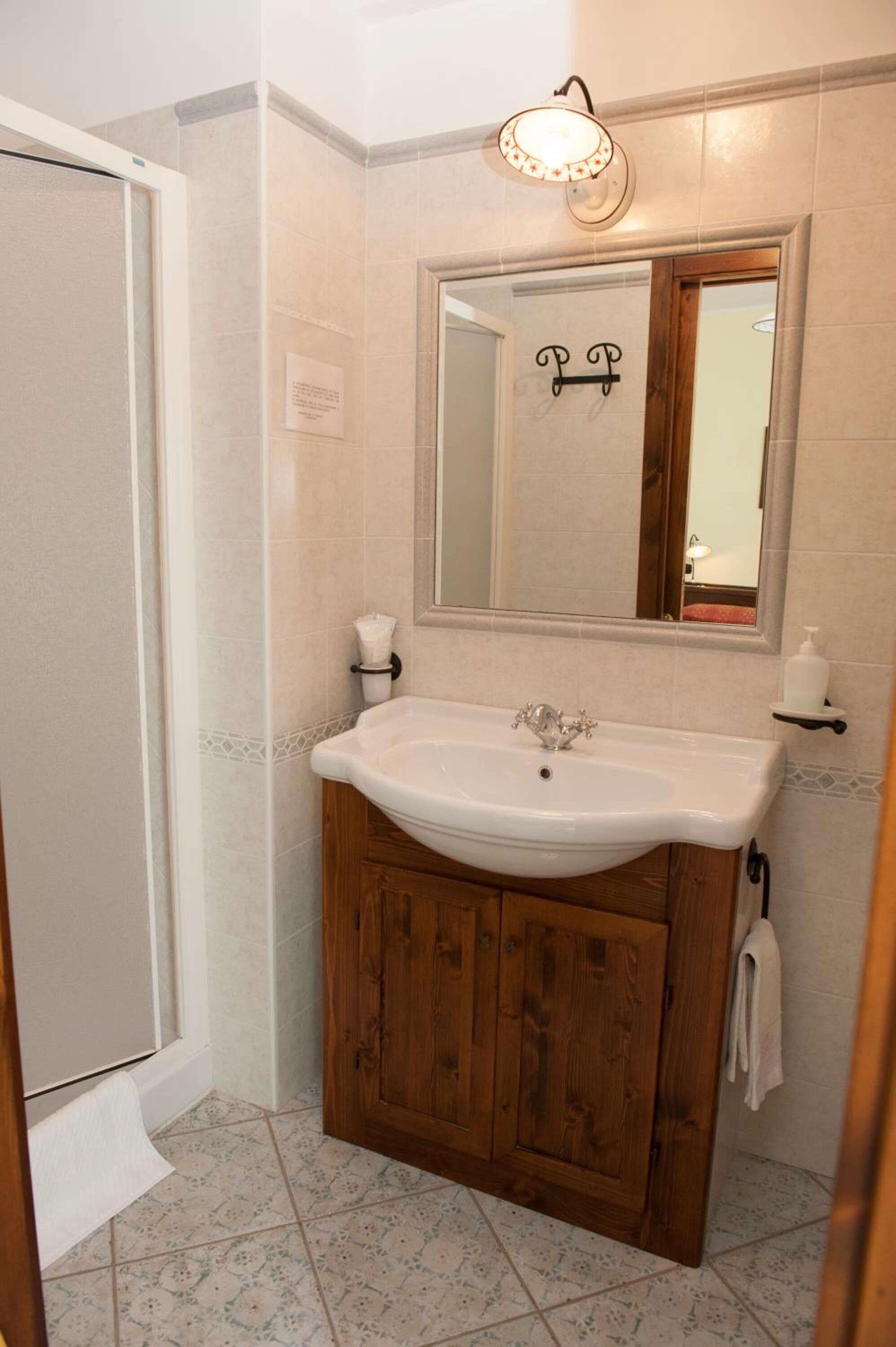 Un baño con tocador de madera, lavamanos blanco, espejo y mampara de ducha.
