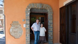 Un homme et une femme se tiennent à l’entrée d’un bâtiment, devant une arche en pierre et une porte en bois.