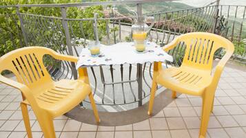 A balcony with two yellow plastic chairs and a table with a pitcher of orange juice.