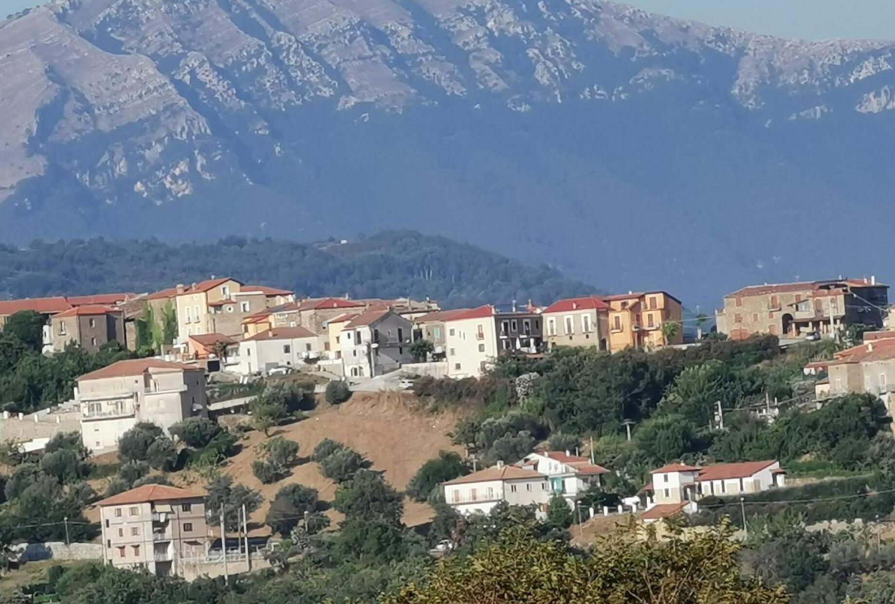 Un asentamiento en una ladera con edificios de tejados rojos, rodeado de vegetación y montañas al fondo.