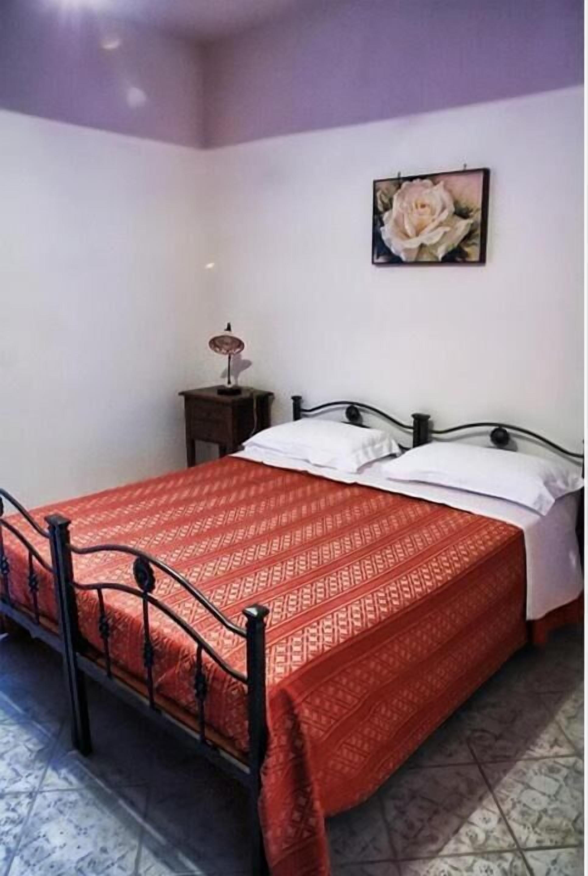 Una cama individual con una colcha estampada, una mesita de noche con lámpara, y un cuadro enmarcado en la pared.