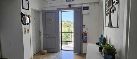 A hallway with a chandelier, a door leading outside, a fire extinguisher, and a small table with plants.