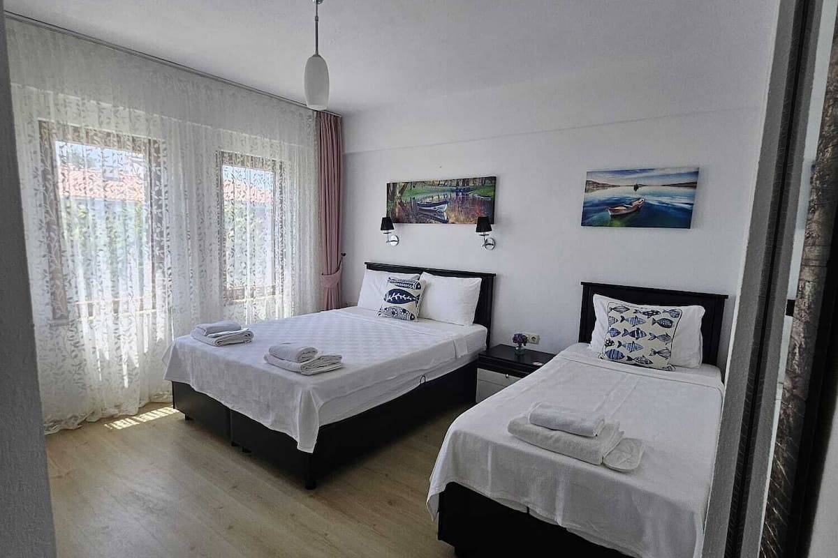 Habitación de hotel con dos camas, una ventana con cortinas, un cuadro en la pared y una lámpara en el techo.