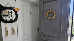 Una puerta gris con un adorno de lazo, una cesta pequeña y un objeto enmarcado en la pared.