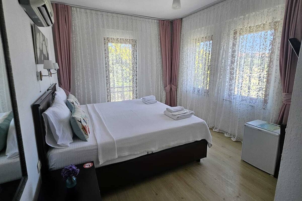 Un dormitorio con cama, cortinas, ventilador de techo y una mesita.