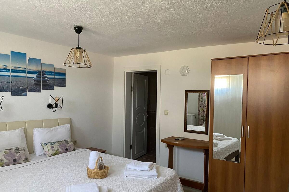 Habitación de hotel con cama, armario de madera, mesita de noche, espejo adosado a la pared y una pared decorada con obras enmarcadas.