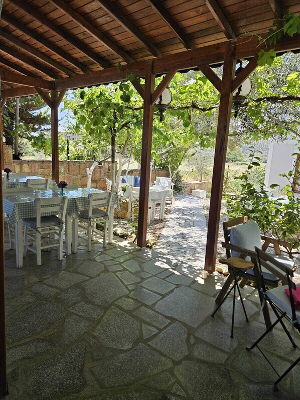 An outdoor patio with stone flooring, white furniture, and a wooden pergola structure. - Alize Otel (Bozcaada)