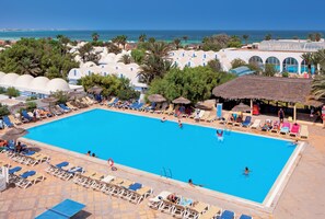 Una piscina grande con sillas de descanso y sombrillas, rodeada de palmeras y una vista despejada del océano.