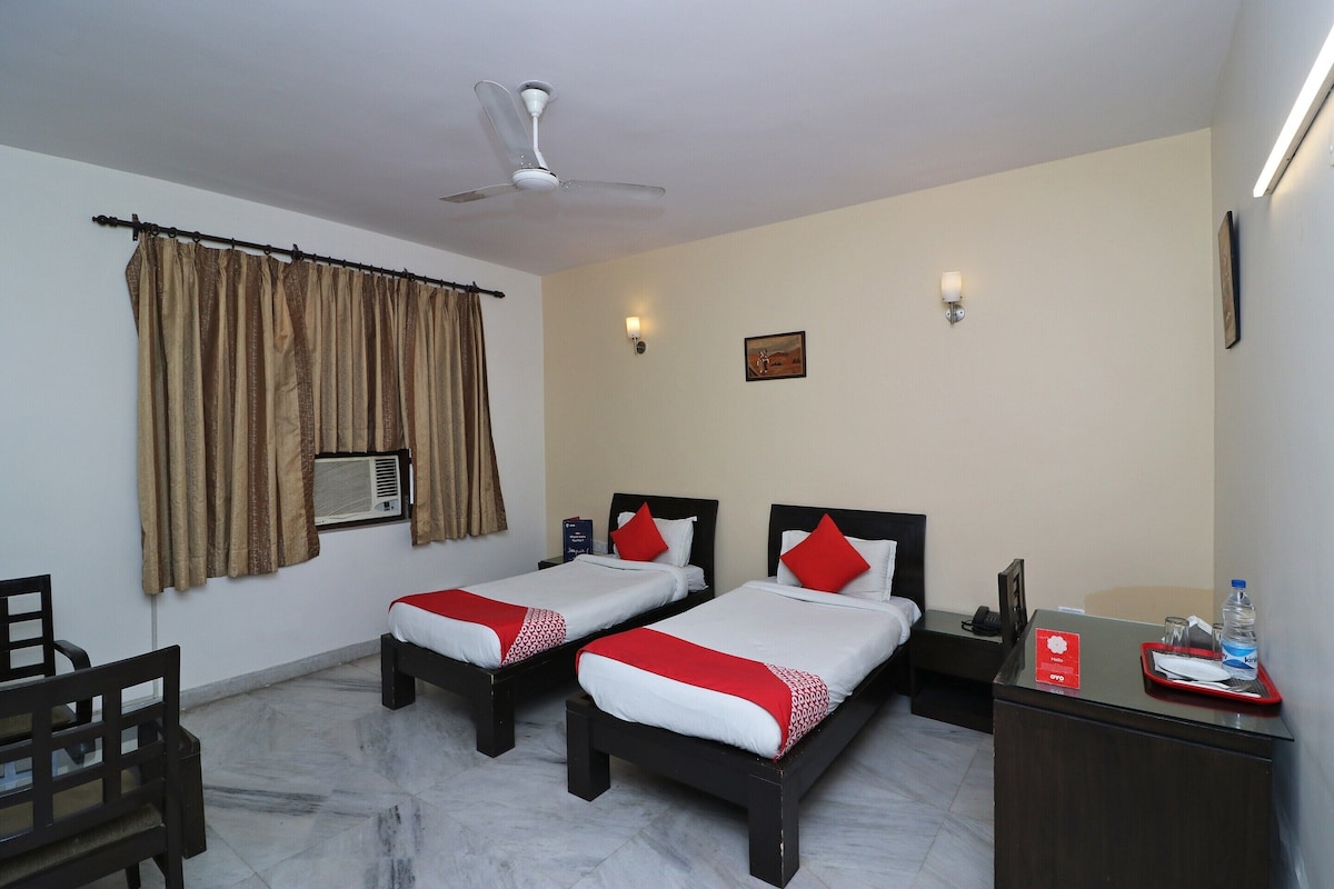 A hotel room with two beds, a ceiling fan, an air conditioning unit, a desk with a tray, and a water bottle.