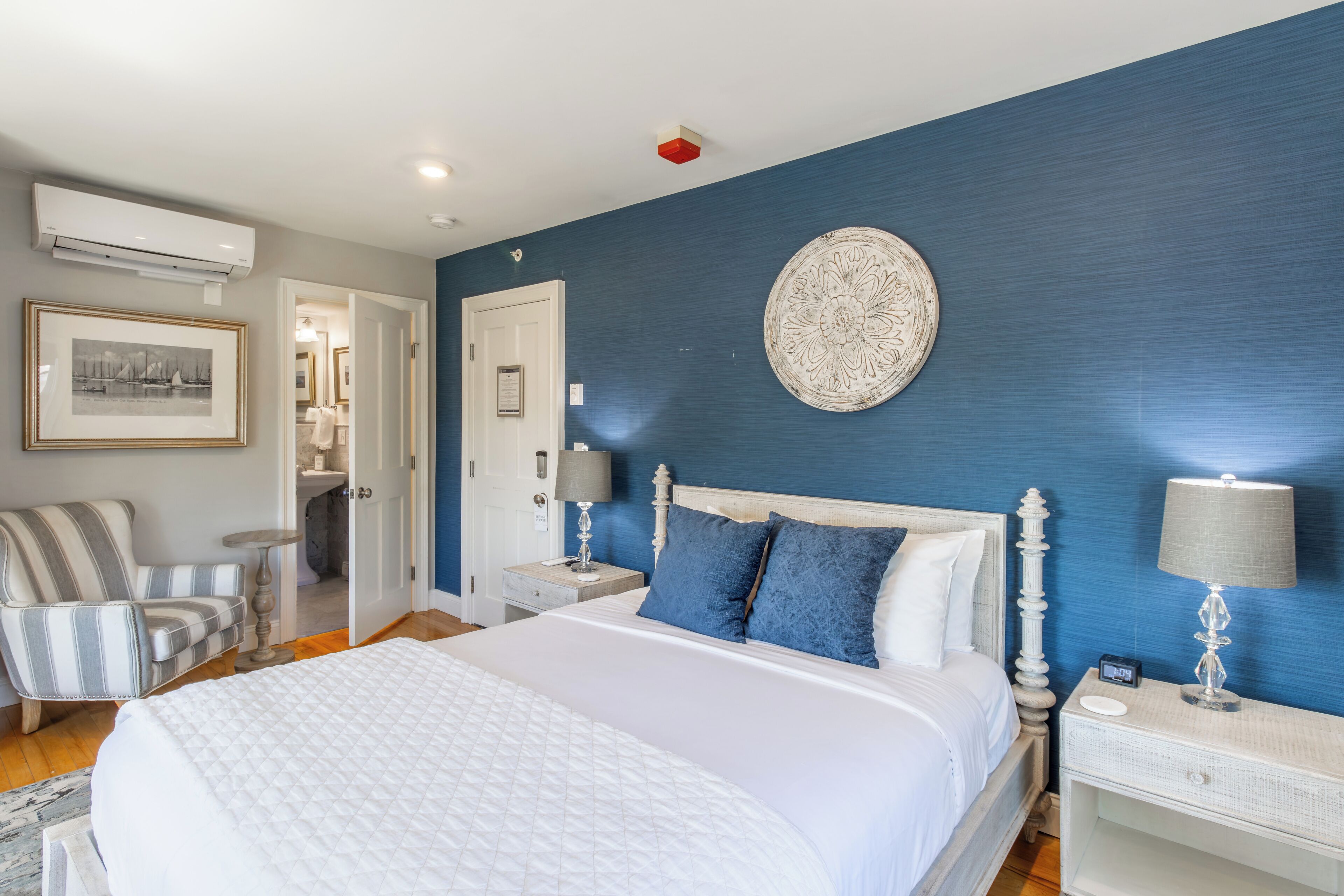 Une chambre à coucher avec un grand lit, une chaise, une table de chevet avec une lampe et une assiette décorative accrochée au mur.
