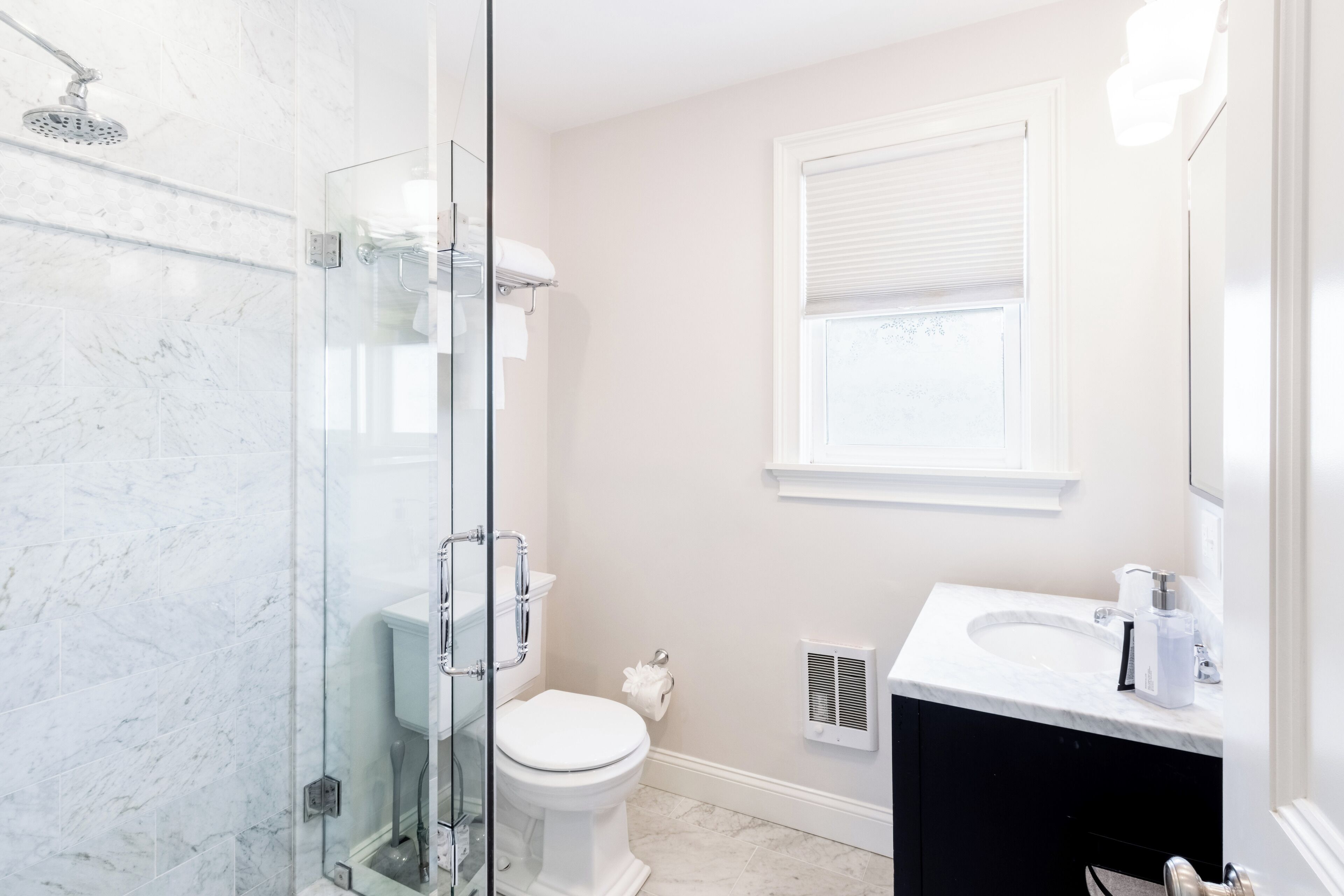 A bathroom with a glass shower enclosure, a toilet, a sink, and a window.