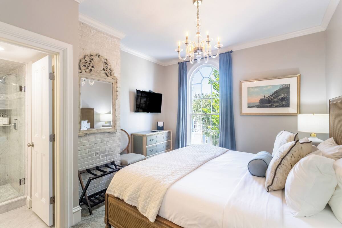A bedroom with a large bed, a chandelier, a television, and a window with curtains.